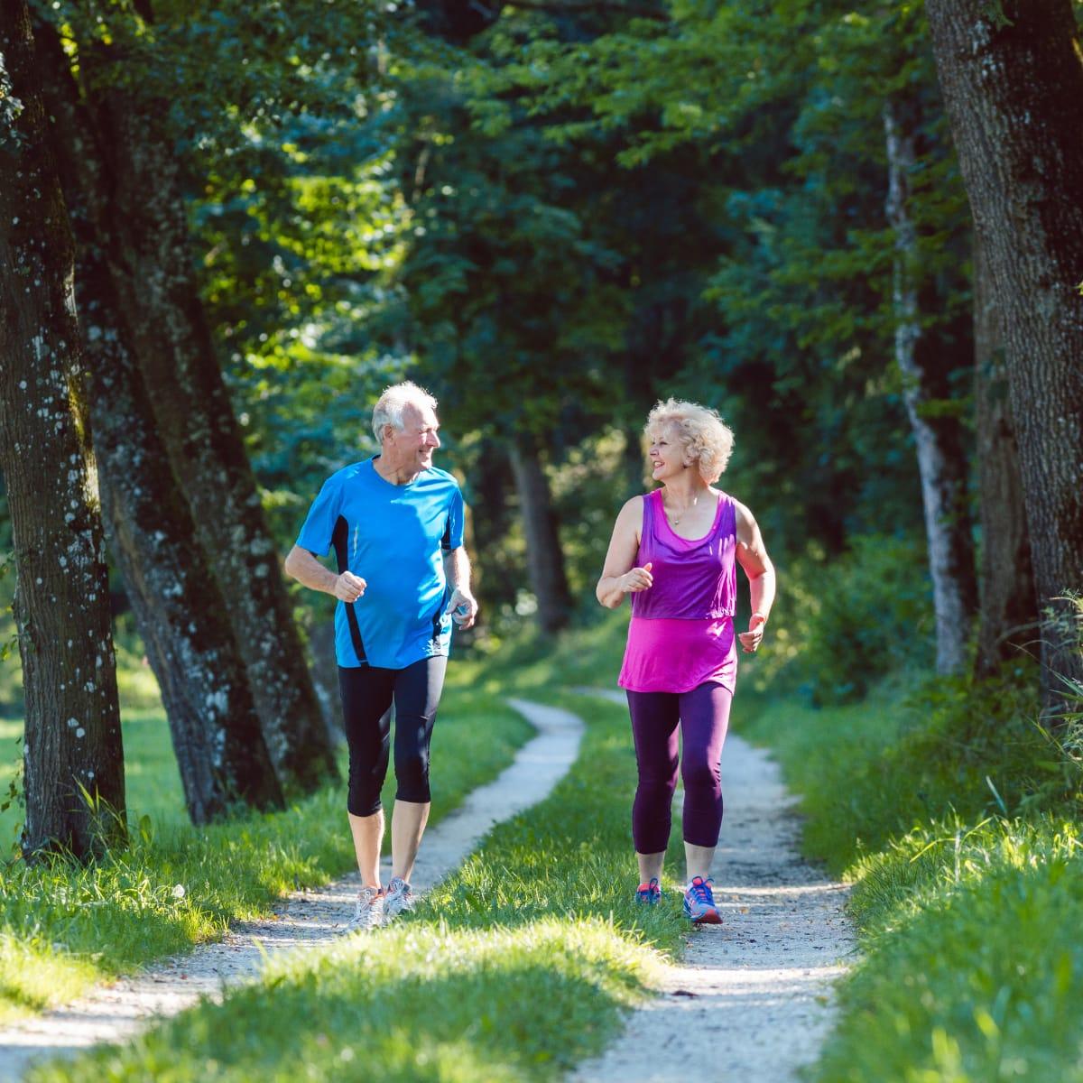 An older couple jogging side by side on a wooded trail