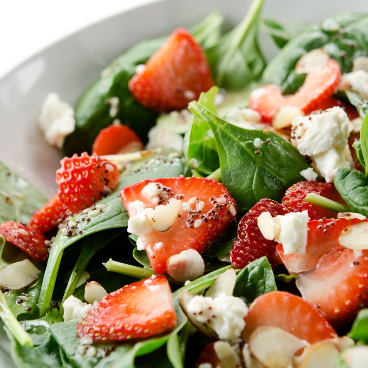 Close-up of a spinach salad with sliced strawberries, crumbled cheese, sliced almonds and poppy seed dressing