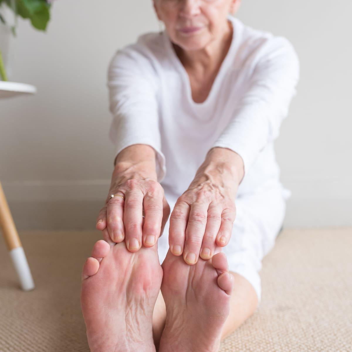 An older woman sitting on the floor reaching forward to hold her bare toes in a seated forward fold