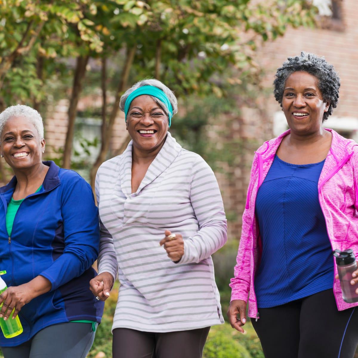 Three smiling older women walking together outdoors in workout clothes
