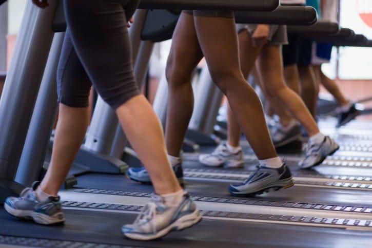 Close-up of several people's legs and sneakers walking on a row of treadmills