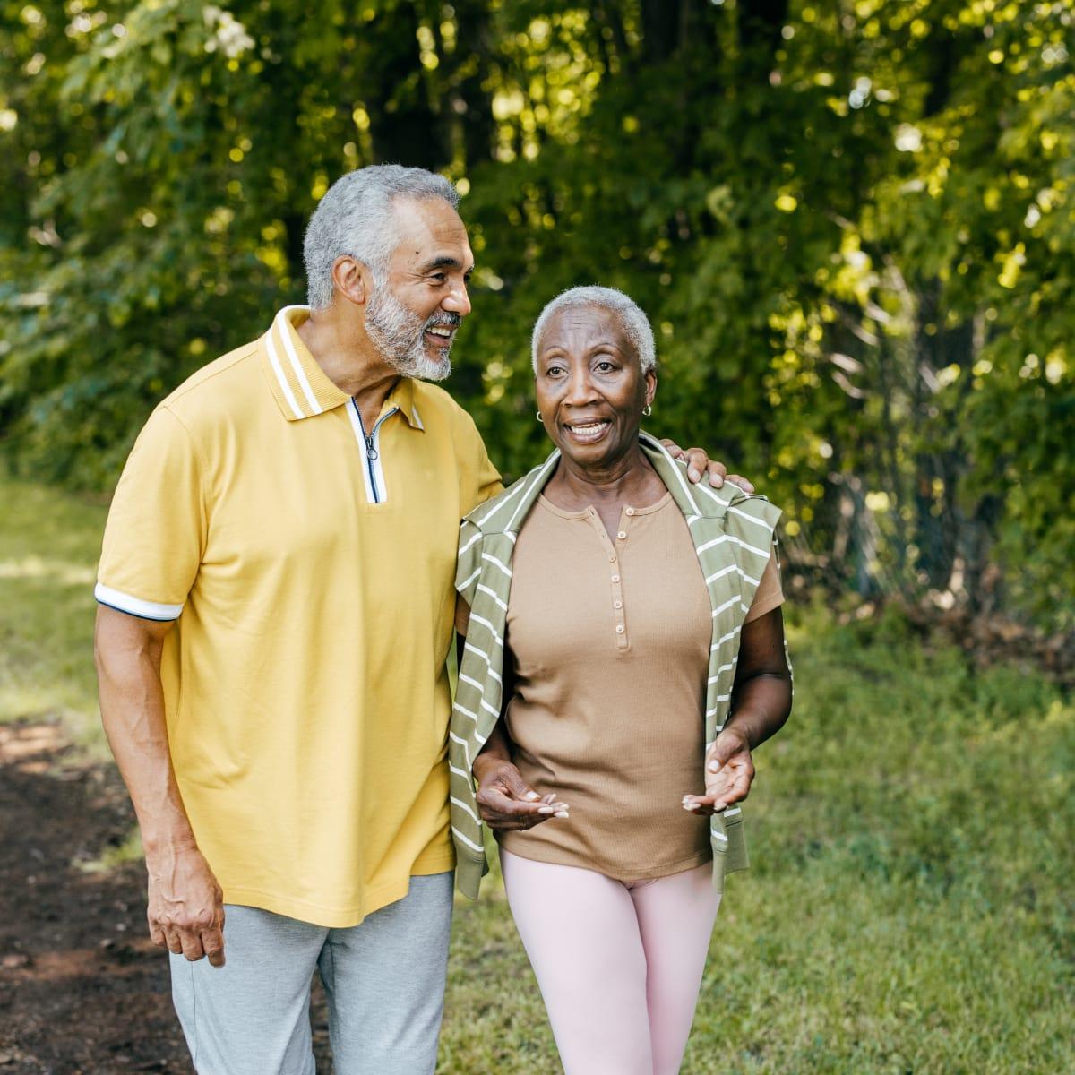 A smiling older couple walking arm in arm along a wooded path
