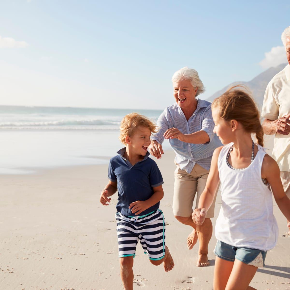 A grandmother running and laughing with her grandchildren along a sunny beach