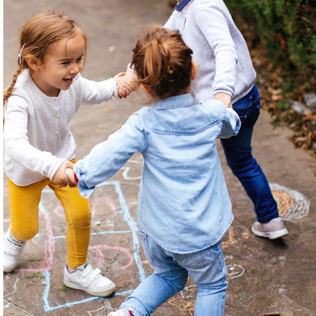 Young children holding hands and playing hopscotch on a chalk-drawn sidewalk