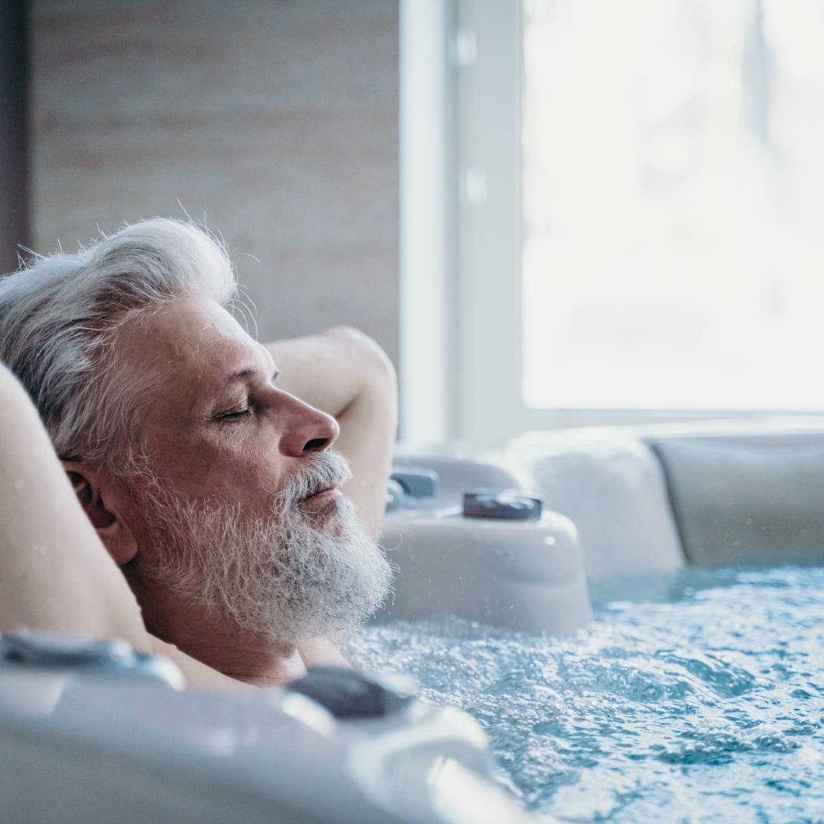 An older man with a gray beard relaxing with his eyes closed in a bubbling hot tub