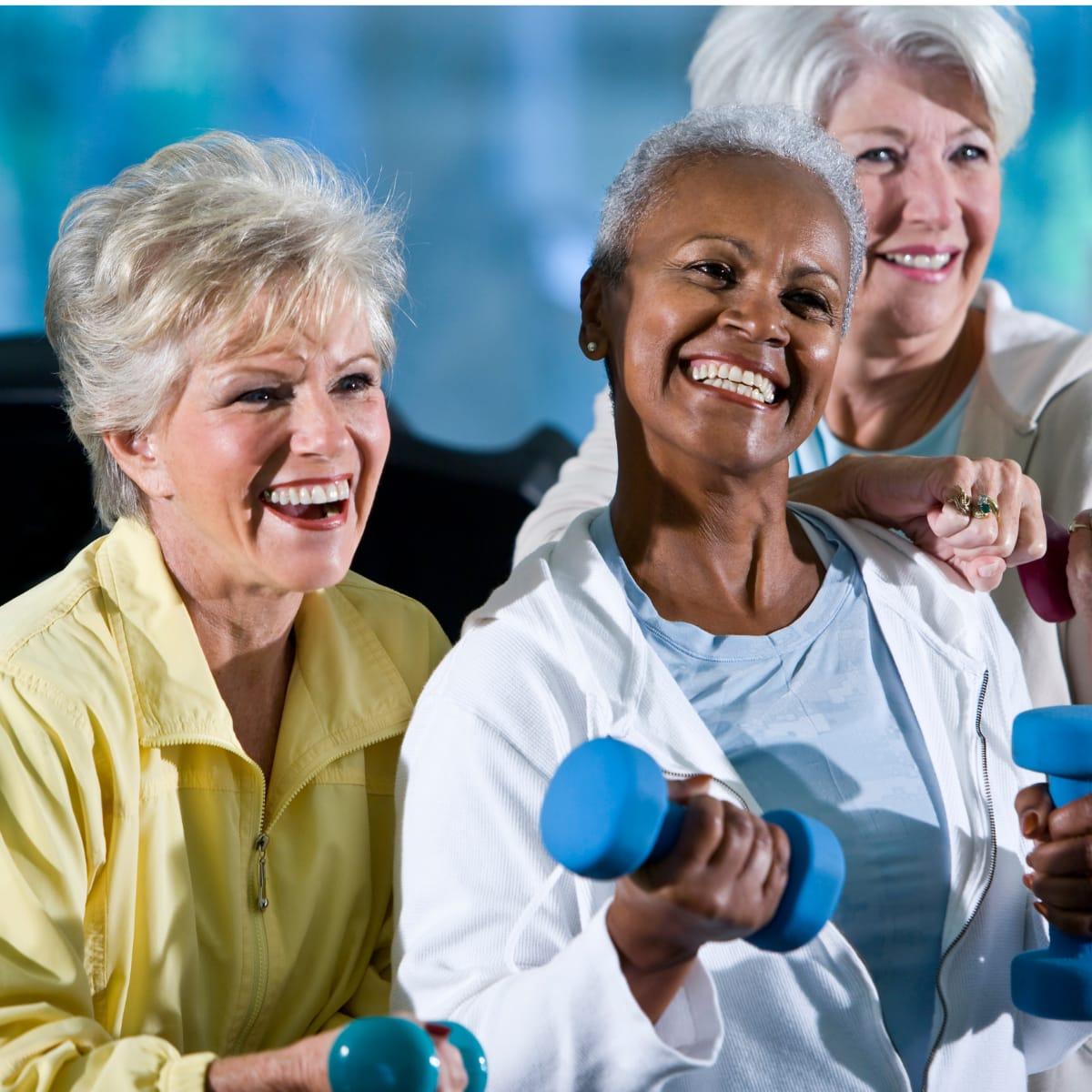 Three smiling older women lifting light dumbbells together in an exercise class