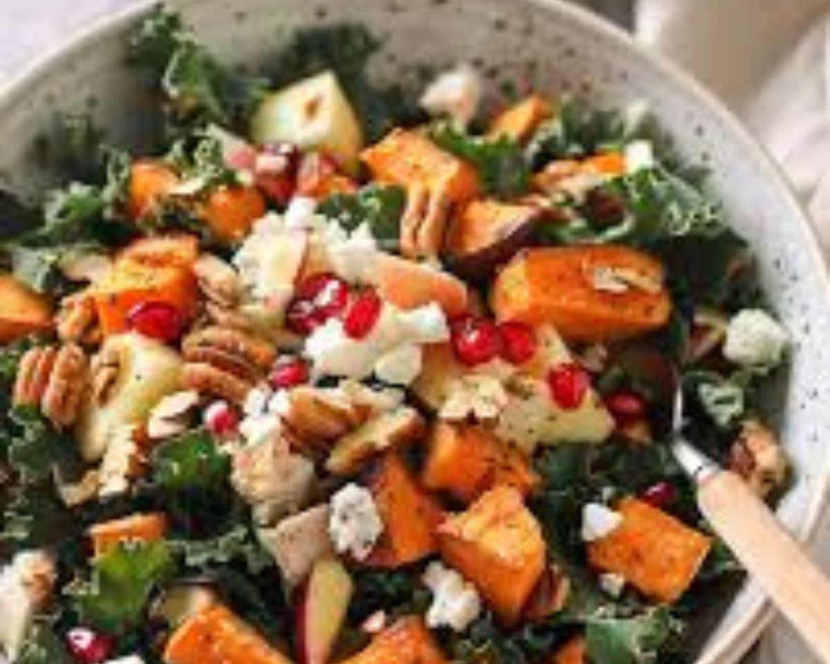 A bowl of roasted sweet potato cubes, apple, pecans, crumbled goat cheese and pomegranate seeds over greens