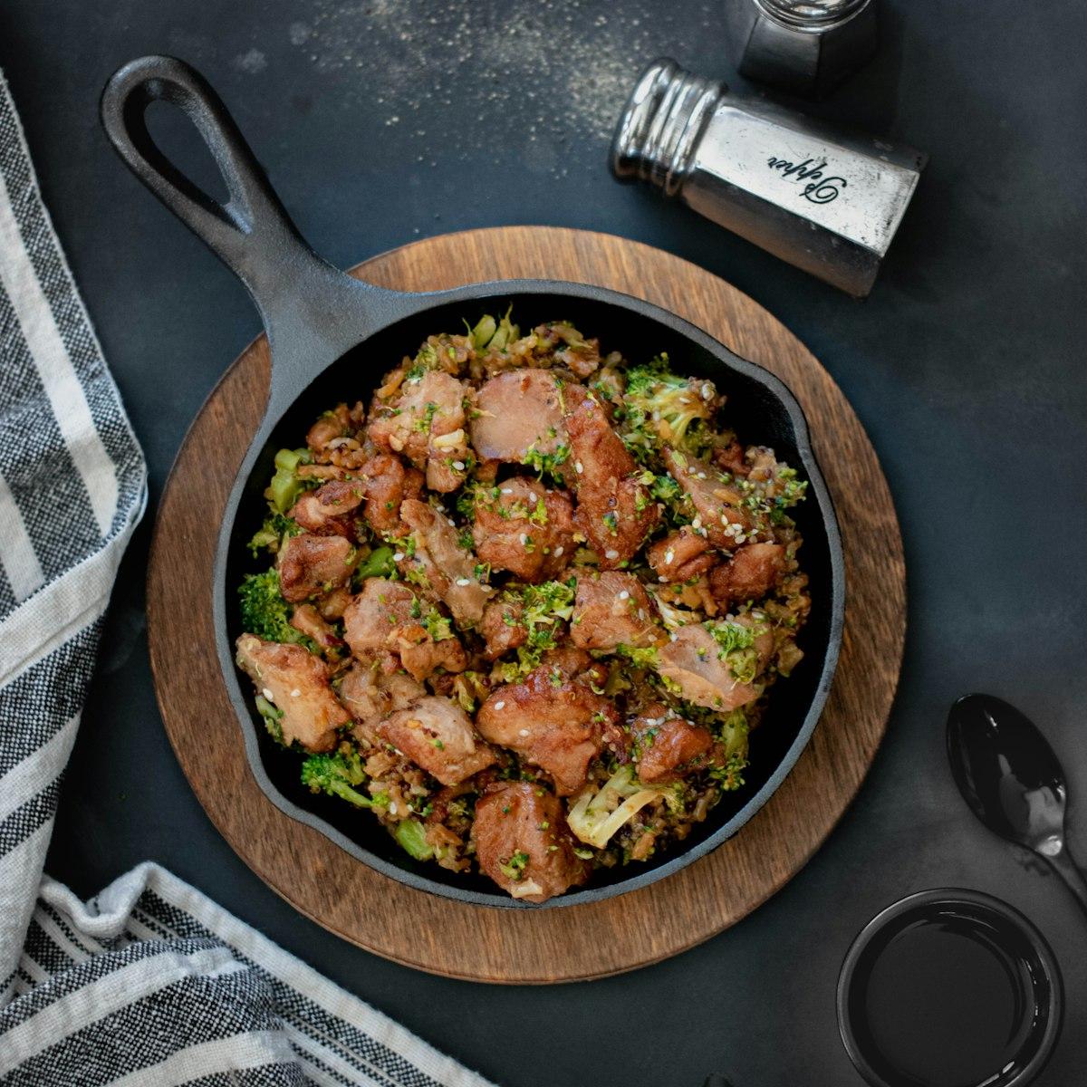 A cast-iron skillet of chicken and broccoli on a wooden board