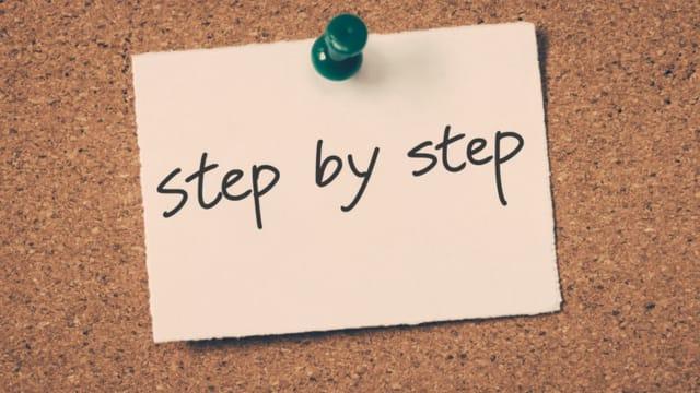 A note reading "step by step" pinned to a cork board