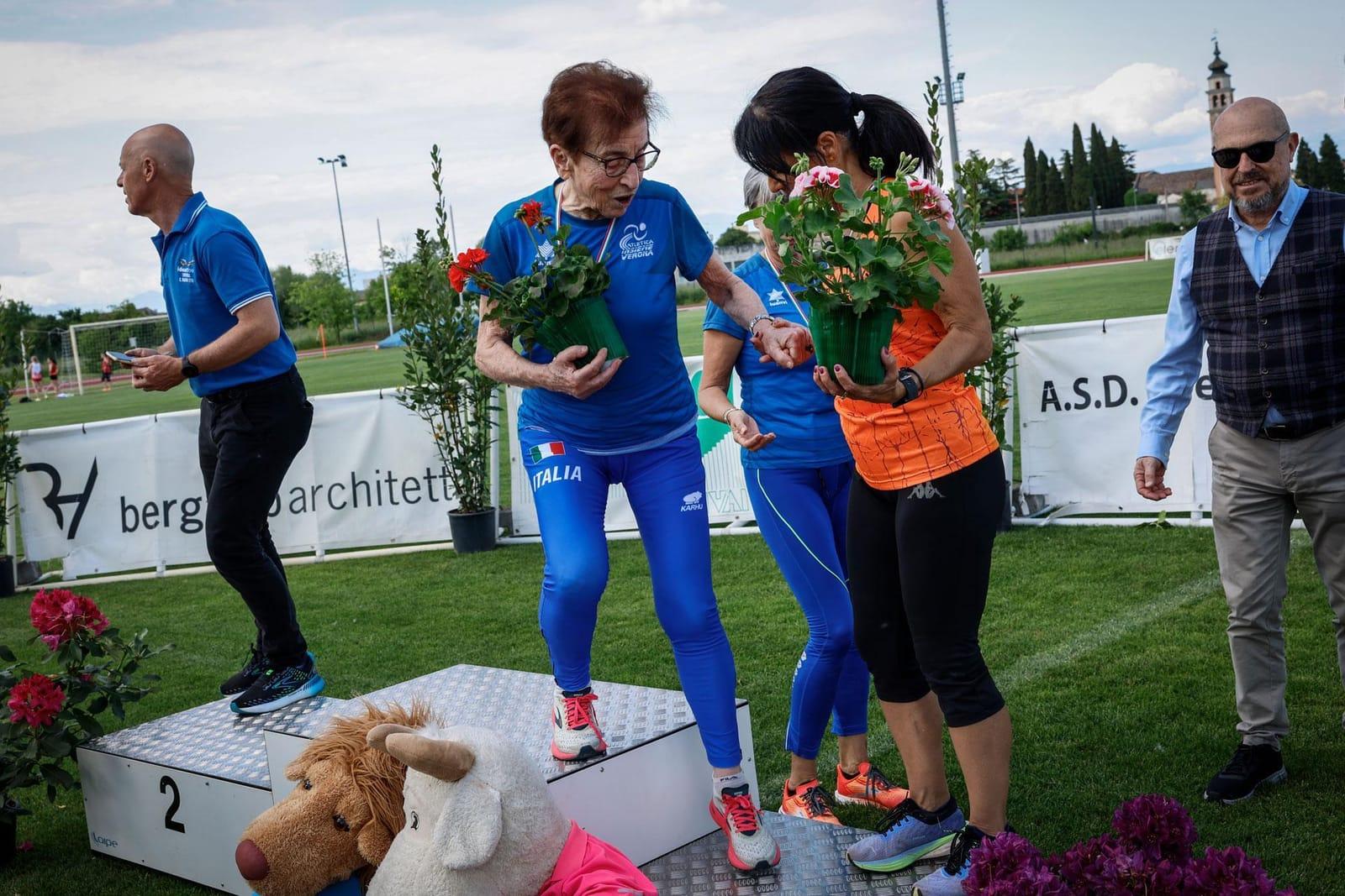 Emma Maria Mazzenga in a blue Italia tracksuit stepping onto a medal podium, holding a potted plant