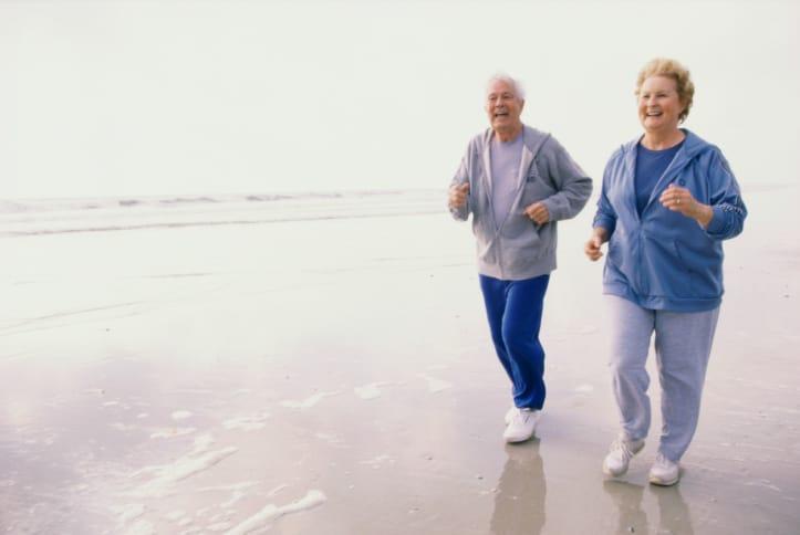 An older couple jogging together along a misty beach
