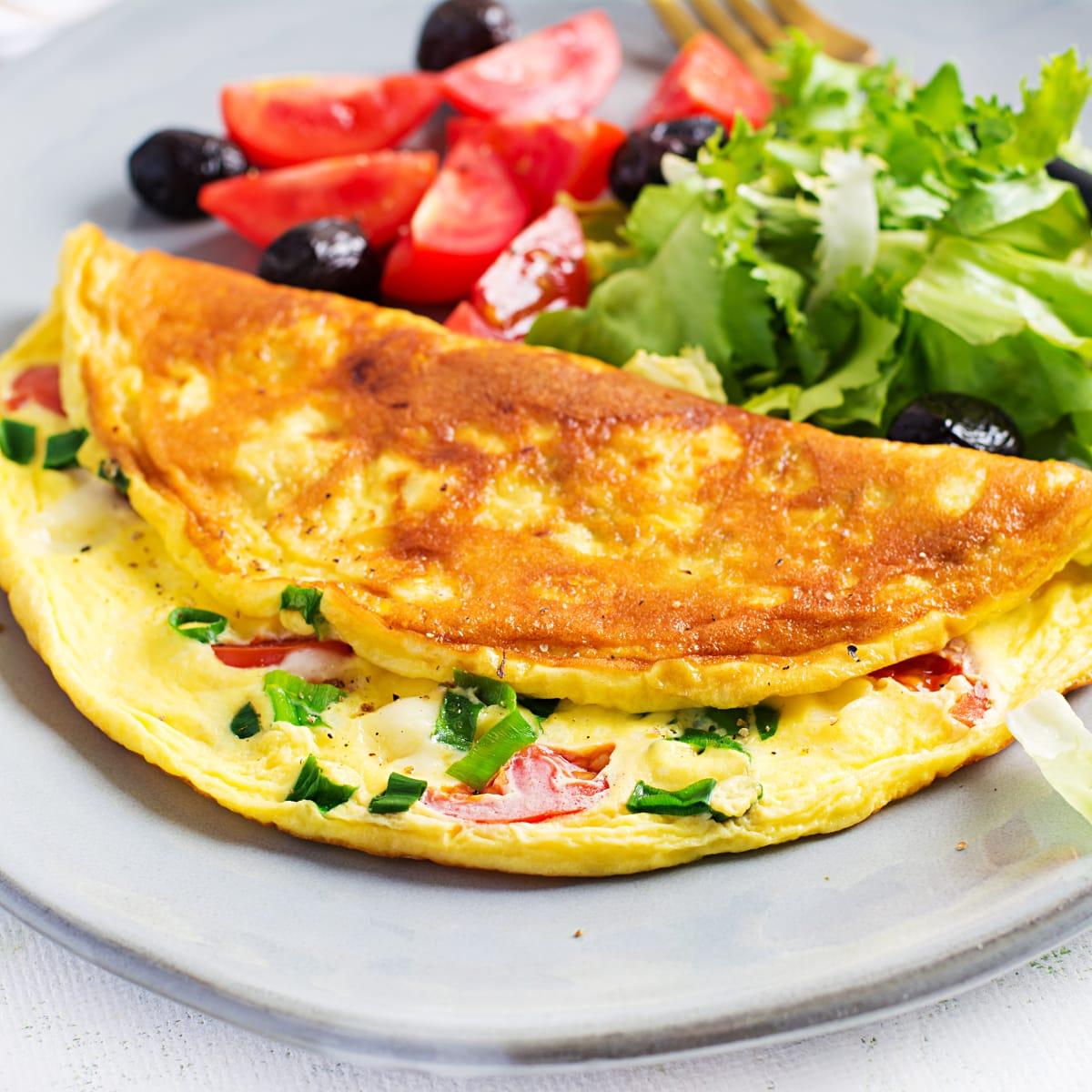 A folded omelet with tomatoes and green onions next to a side salad