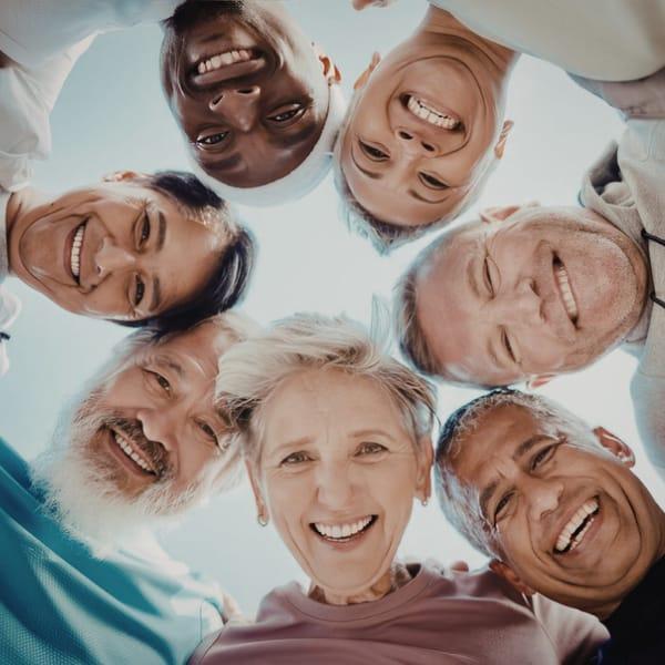 A circle of smiling older adults looking down at the camera with their arms around each other
