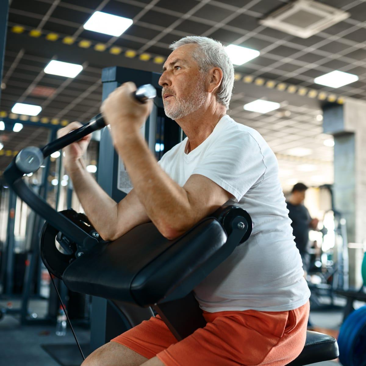 An older man working hard on an arm curl machine in a gym