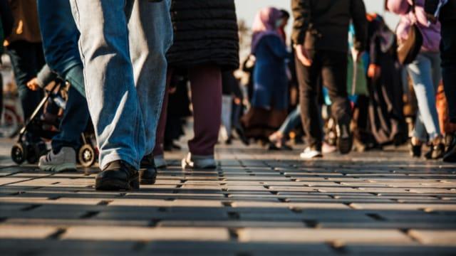 Close-up of many people's legs and feet walking across a busy paved street