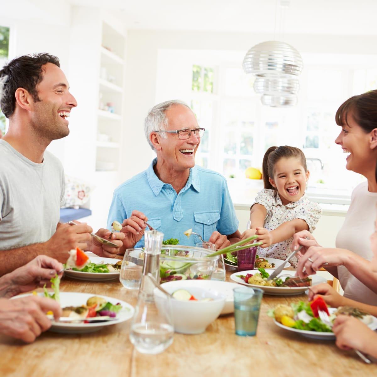 Three generations of a family laughing together over a healthy dinner at the kitchen table