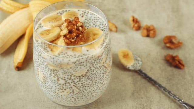 A glass of chia seed pudding topped with banana slices and walnuts