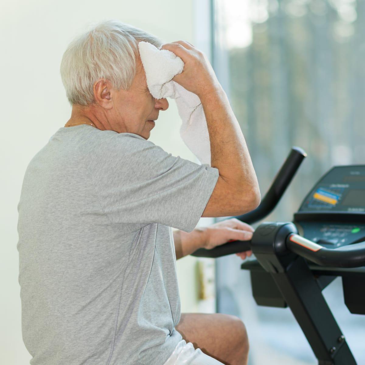 An older man wiping his forehead with a towel while riding a stationary bike