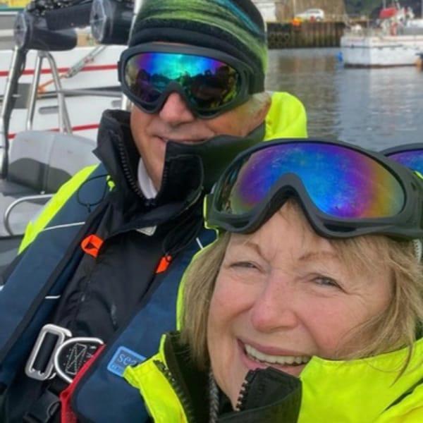 Brenda and her husband John smiling in ski goggles and bright jackets on a boat