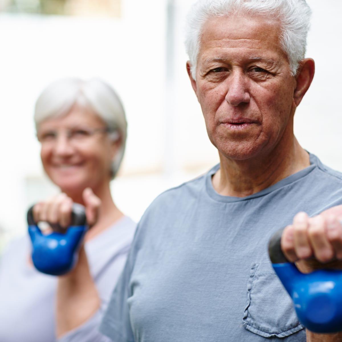 An older man and woman lifting blue kettlebells
