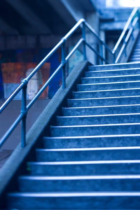 A concrete outdoor staircase with a metal handrail, lit in cool blue tones