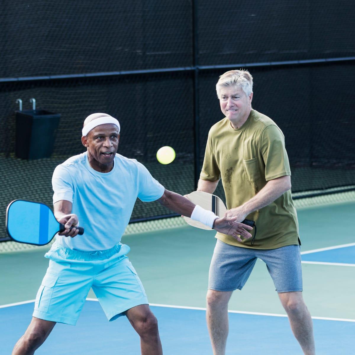 Two older men playing pickleball together, one reaching to hit the ball with his paddle