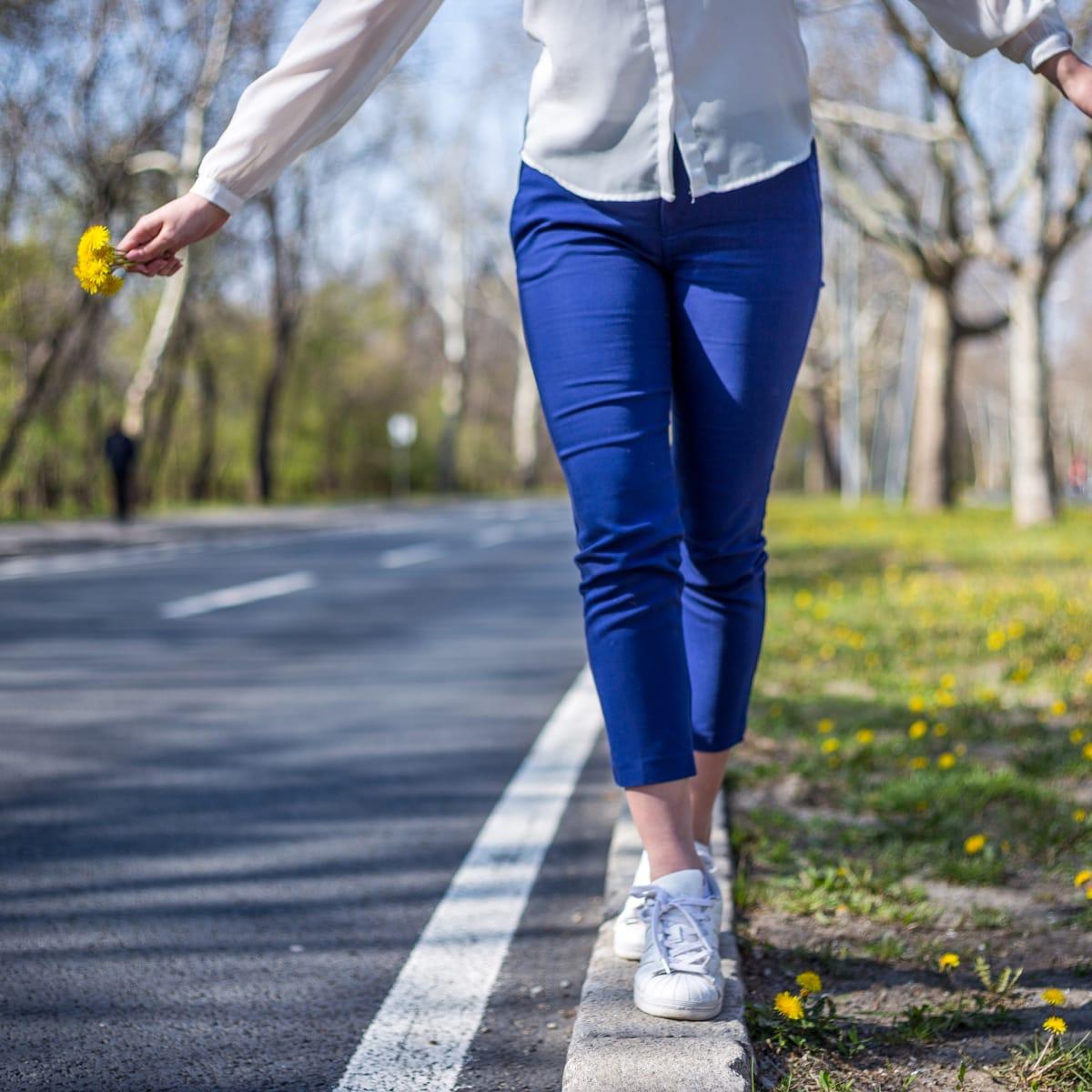 A woman in blue pants and sneakers walking heel to toe along a painted line at the edge of a park road