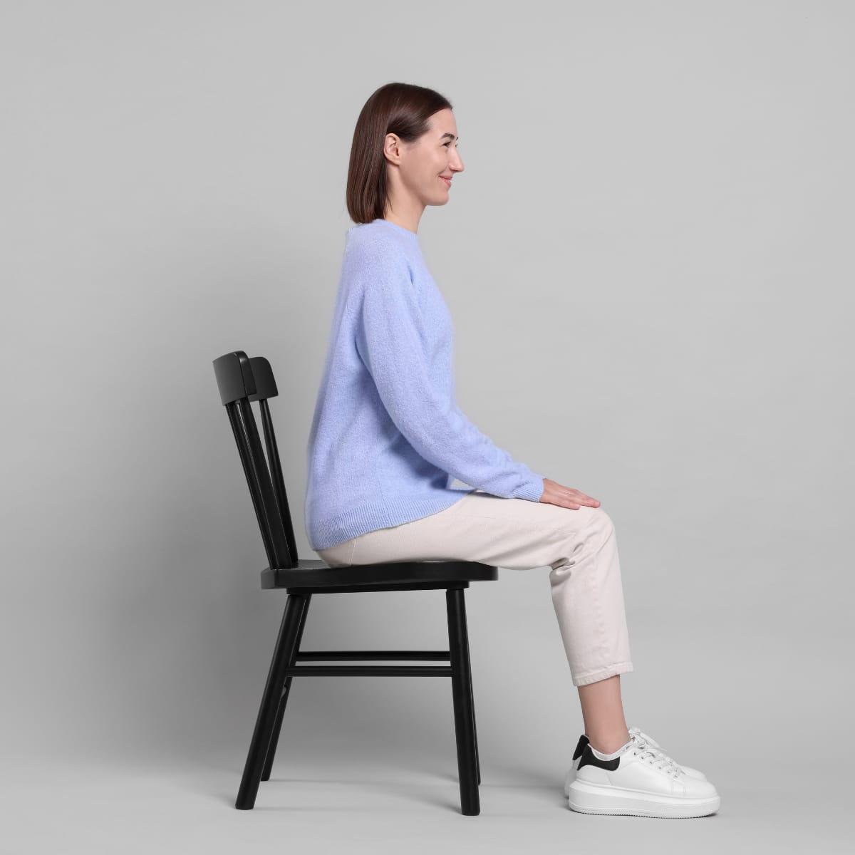A woman sitting tall at the edge of a wooden chair with her feet flat on the floor