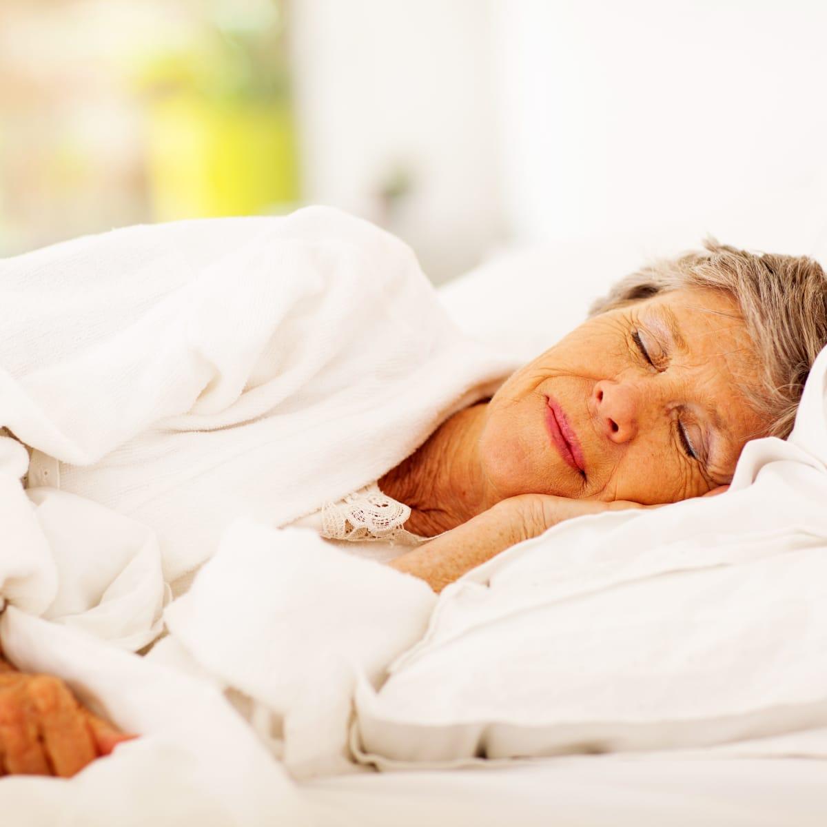 An older woman sleeping peacefully under a white comforter