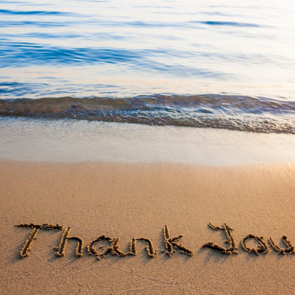 The words "Thank You" written in the sand at the edge of the ocean