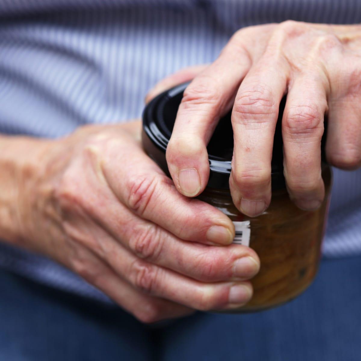 An older person's hands twisting open the lid of a glass jar