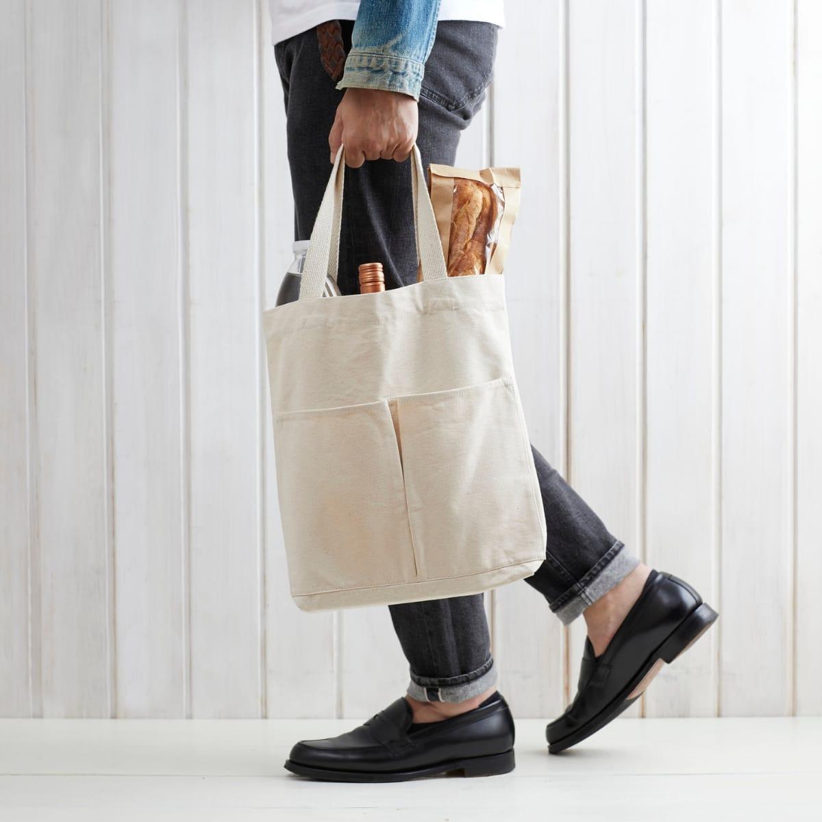 A person walking while carrying a loaded canvas grocery tote in one hand