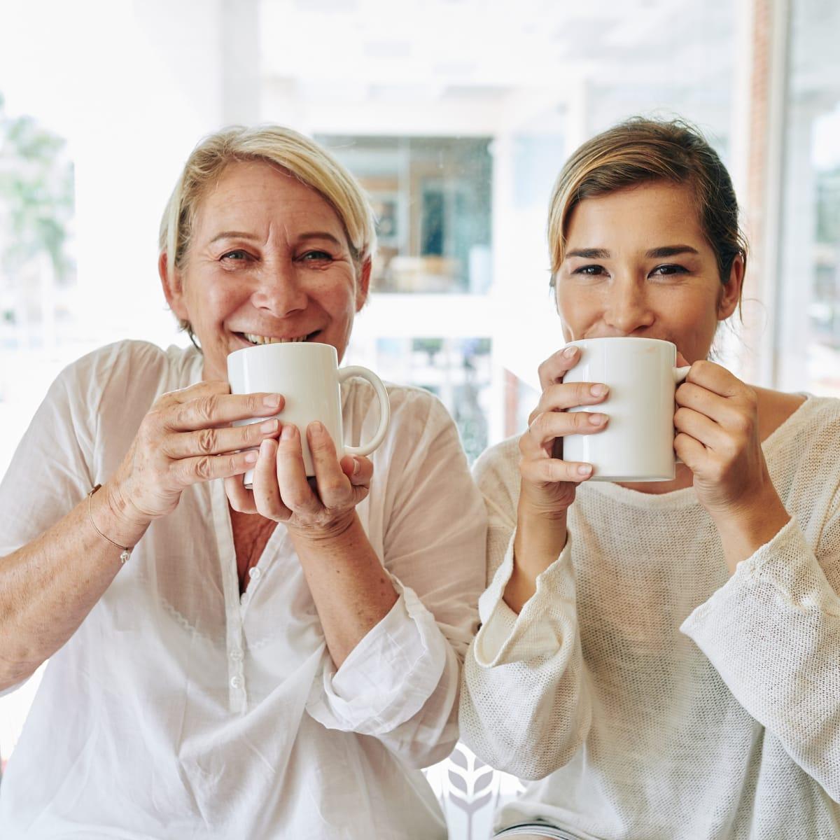 An older woman and a younger woman smiling over white coffee mugs