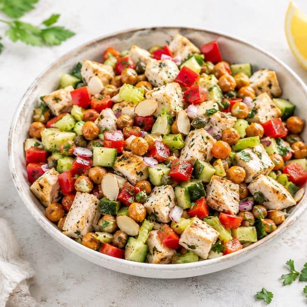 A bowl of chopped chicken salad with roasted chickpeas, cucumber, red bell pepper, sliced almonds and parsley