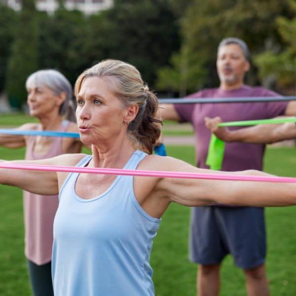 A group of older adults outdoors pulling resistance bands across their chests