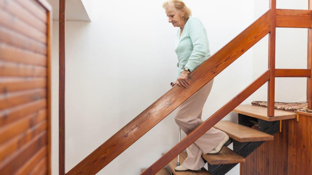 An older woman walking down a wooden staircase, holding the railing
