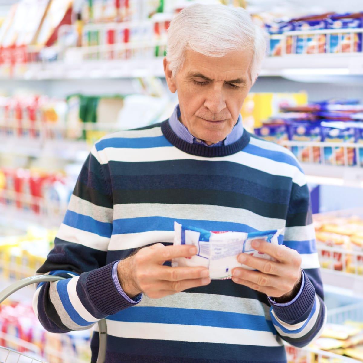 An older man in a striped sweater reading the label on a package in a grocery aisle