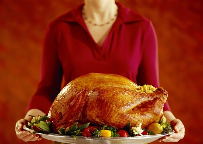 A person holding a roast turkey on a platter garnished with herbs and vegetables