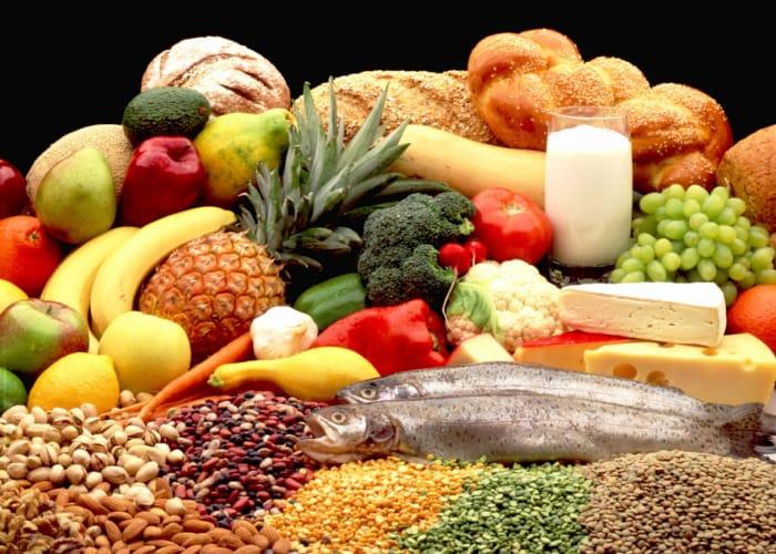 A spread of whole foods including fruit, vegetables, fish, cheese, bread, nuts, beans and lentils