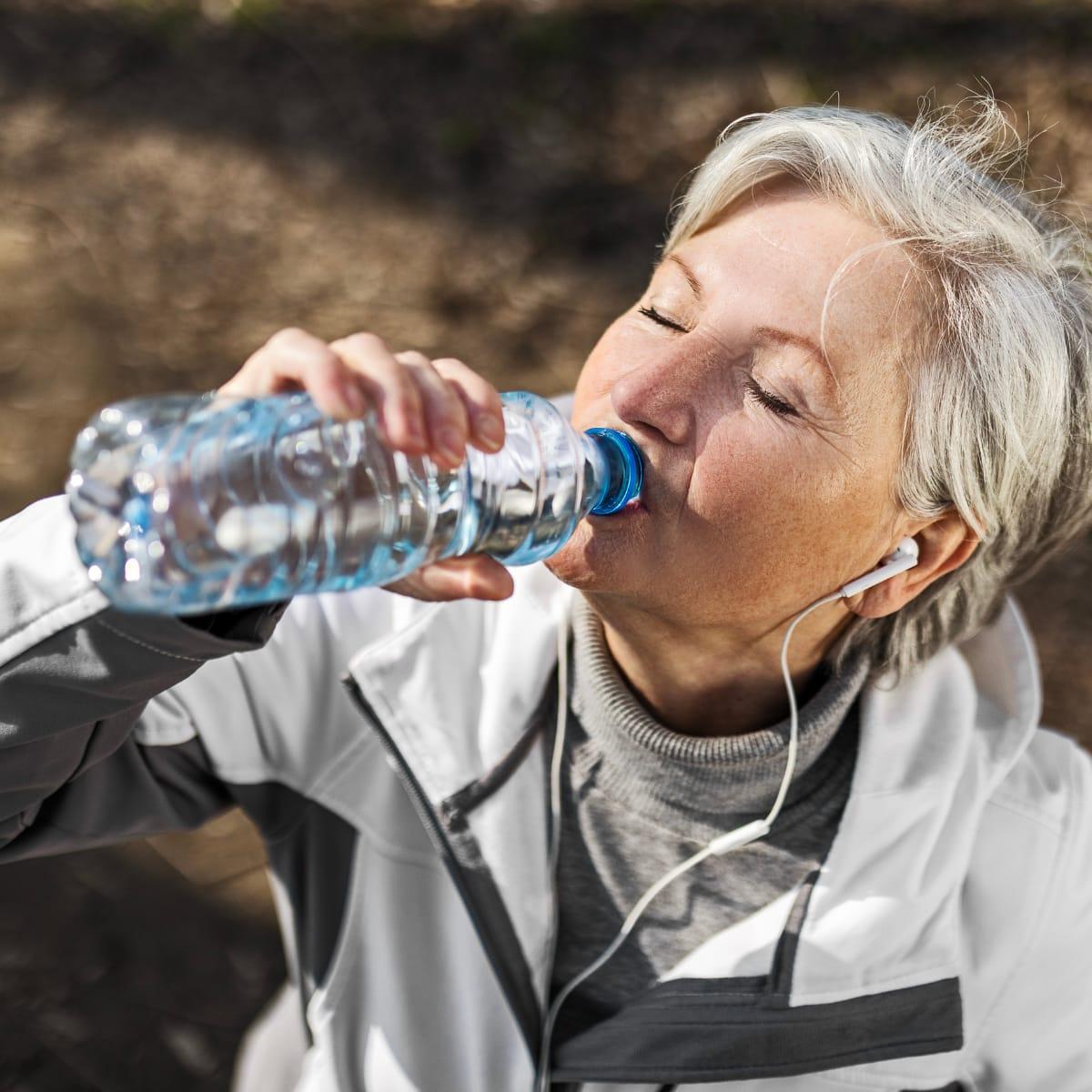 An older woman in a running jacket drinking from a water bottle outdoors