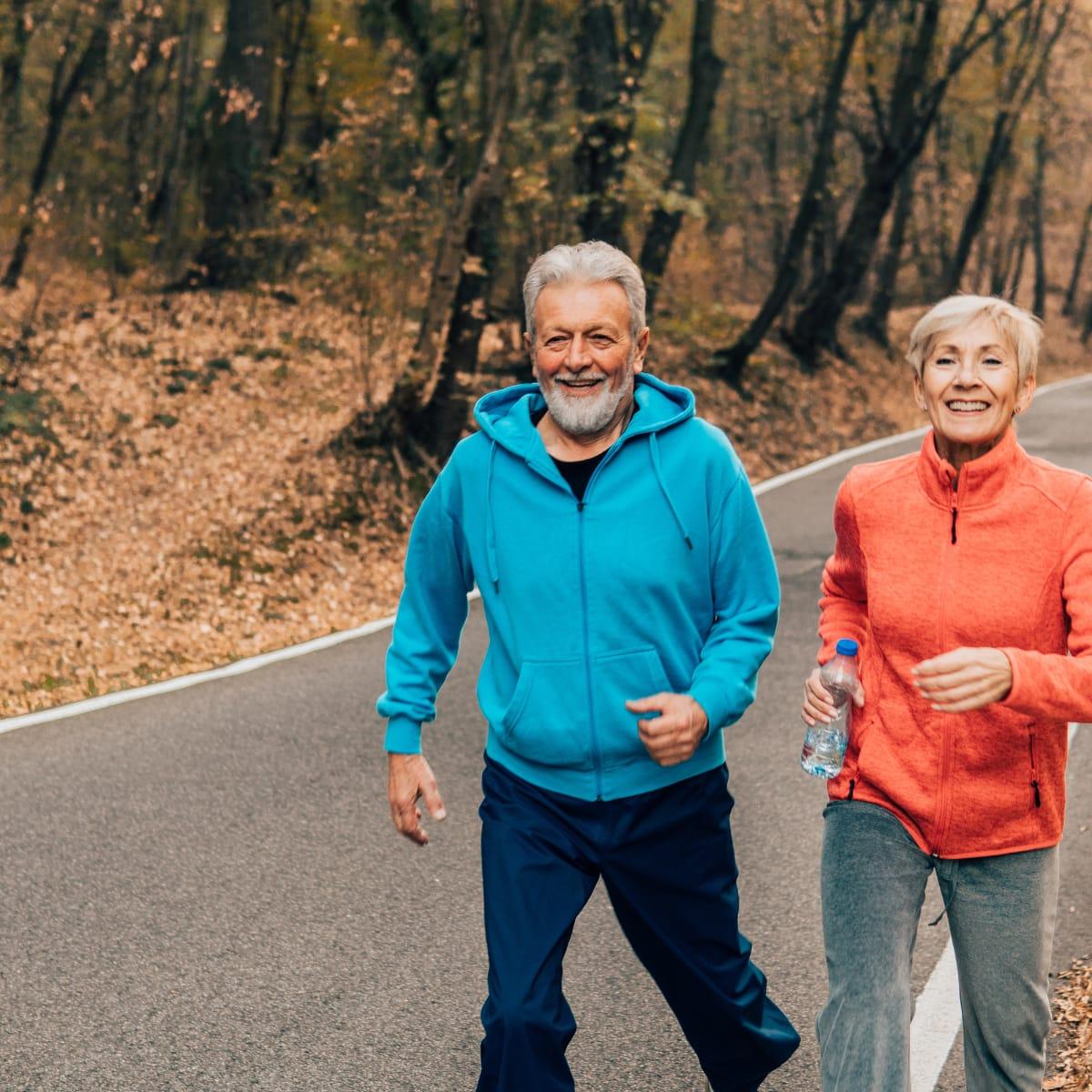 An older couple walking briskly together along a wooded road in autumn