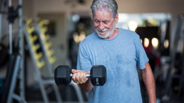 A smiling older man doing a dumbbell curl in a gym