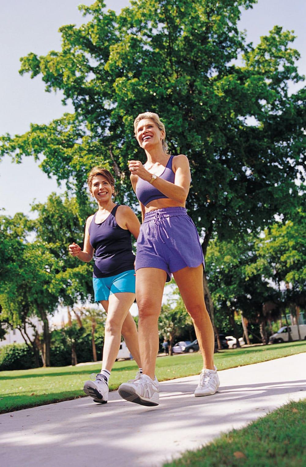 Two women walking briskly together on a tree-lined path