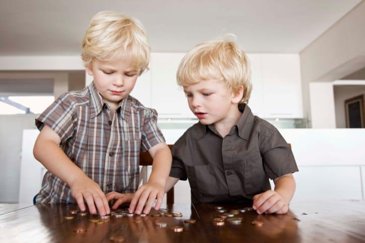 Two young twin brothers counting coins at a table