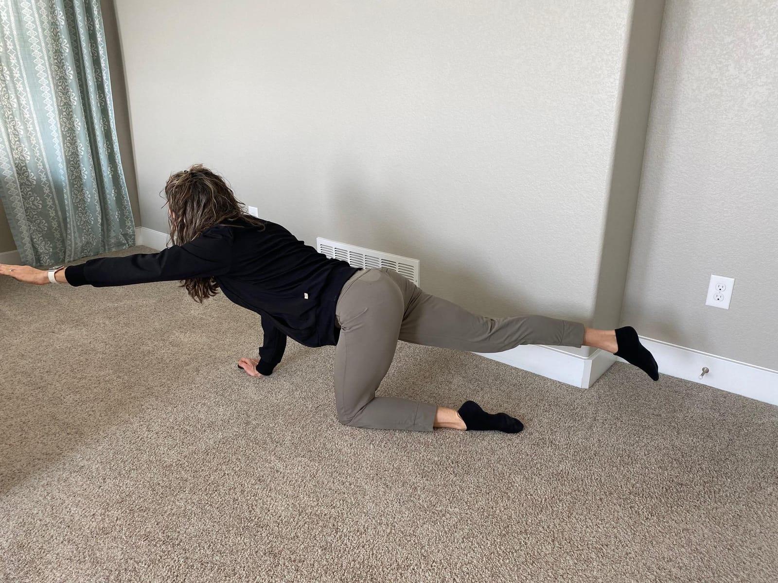 A woman on her hands and knees extending one arm forward and the opposite leg back