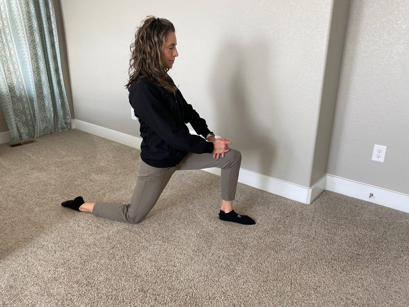 A woman in a kneeling lunge, back knee on the floor and front knee bent, stretching the front of her hip
