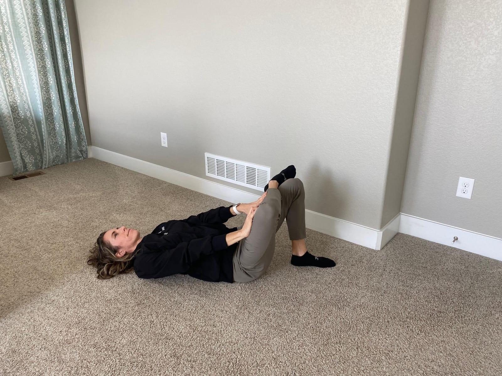 A woman lying on her back with one ankle crossed over the opposite knee in a figure 4 stretch