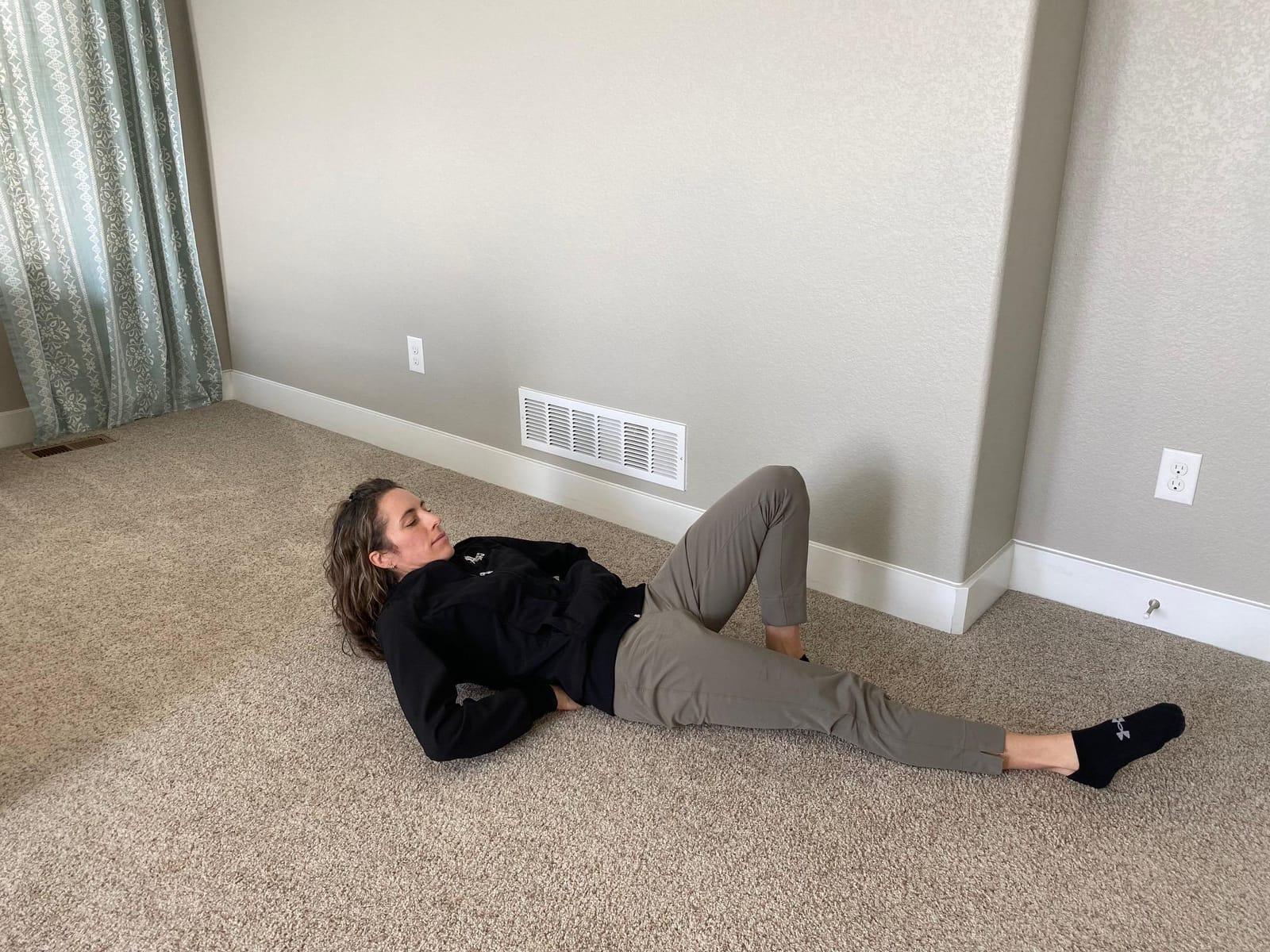 A woman lying on her back with one knee bent and one leg straight, lifting her head and shoulders slightly off the floor