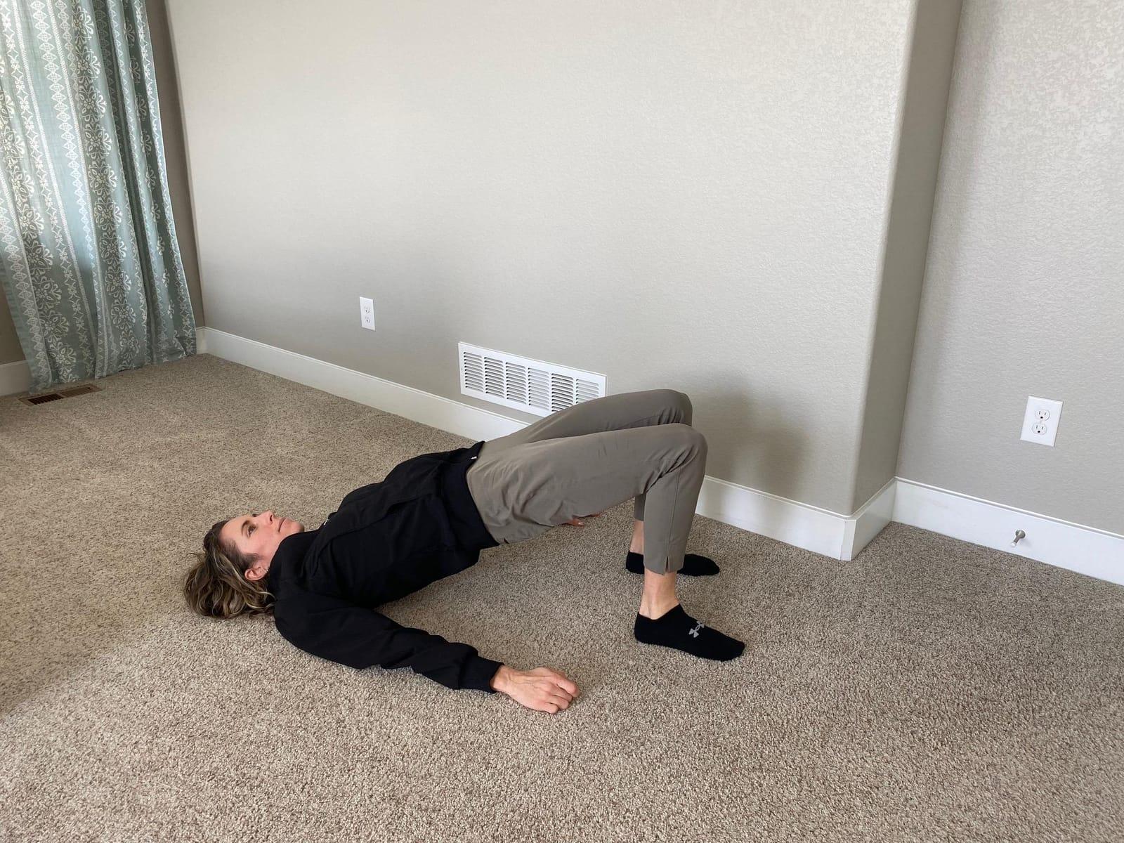 A woman lying on her back with knees bent, lifting her hips into a bridge
