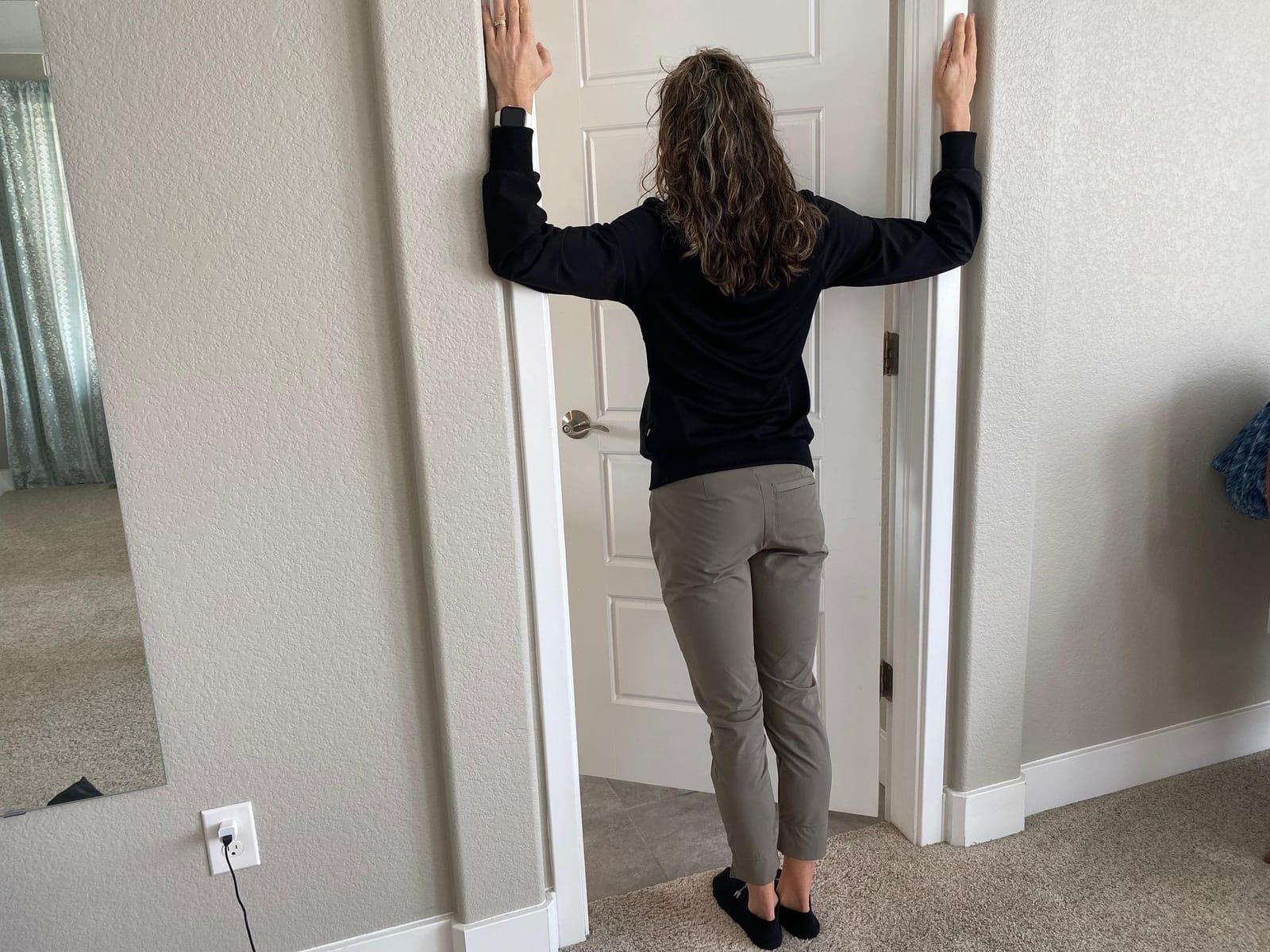 A woman standing in a doorway with her hands on the door frame, stretching her chest